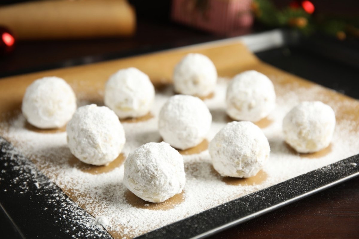 Snowball cookies dusted with powdered sugar on a parchment-lined baking sheet
