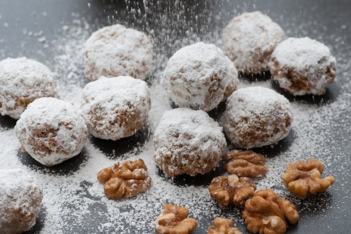 Snowball cookies rolled in powdered sugar next to walnuts