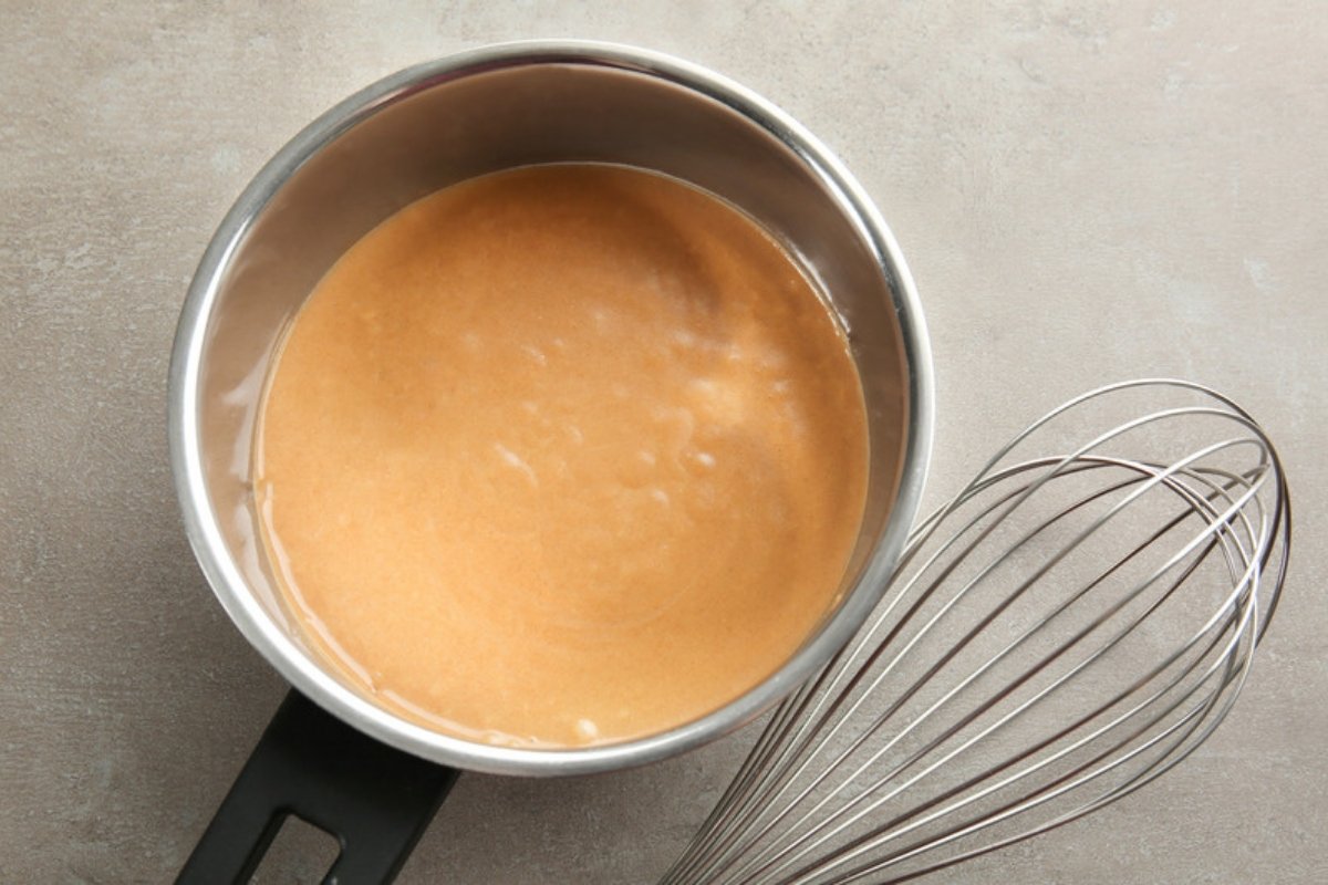 Turkey gravy in a saucepan next to a whisk