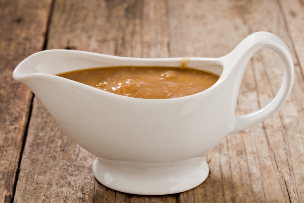 White gravy boat filled with turkey gravy on a wooden table
